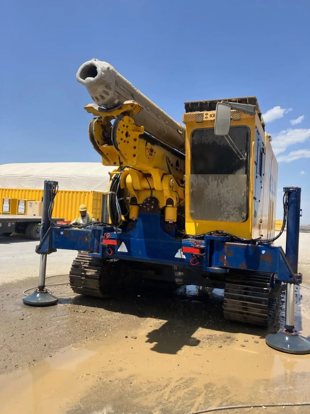 Yellow industrial machine on tracks with extended boom and stabilizing legs in a paved work area