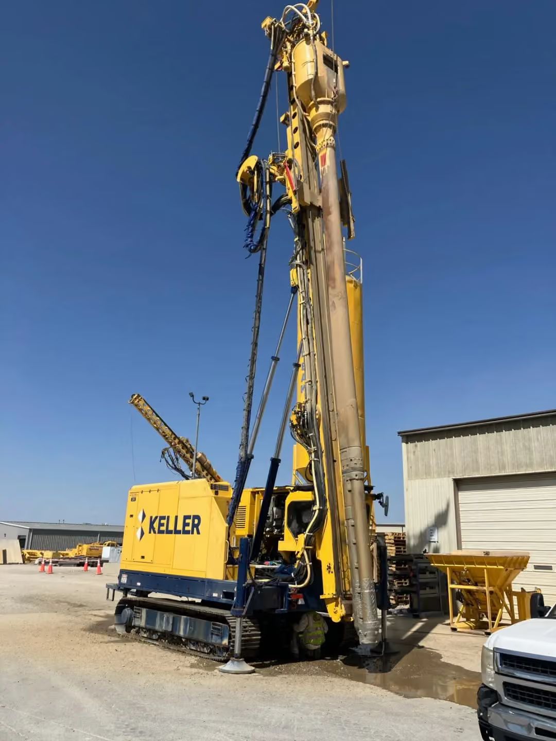 Yellow Keller drilling rig on a construction site next to a building and parked vehicle