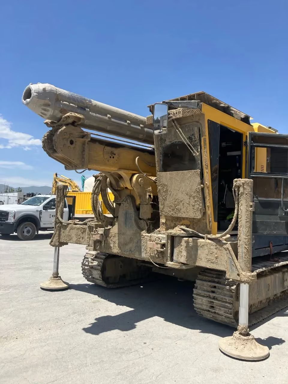 Yellow drilling rig on a construction site with extended auger arms and stabilizing jacks.