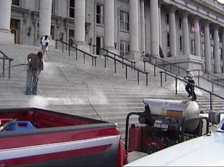 People climbing wide courthouse steps beside parked cars and a railing in the foreground