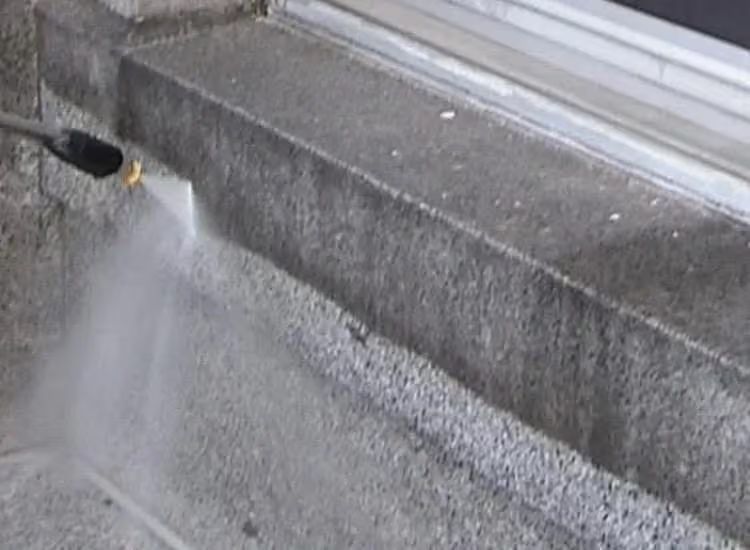 Pressure washer nozzle spraying water onto a concrete curb and sidewalk.