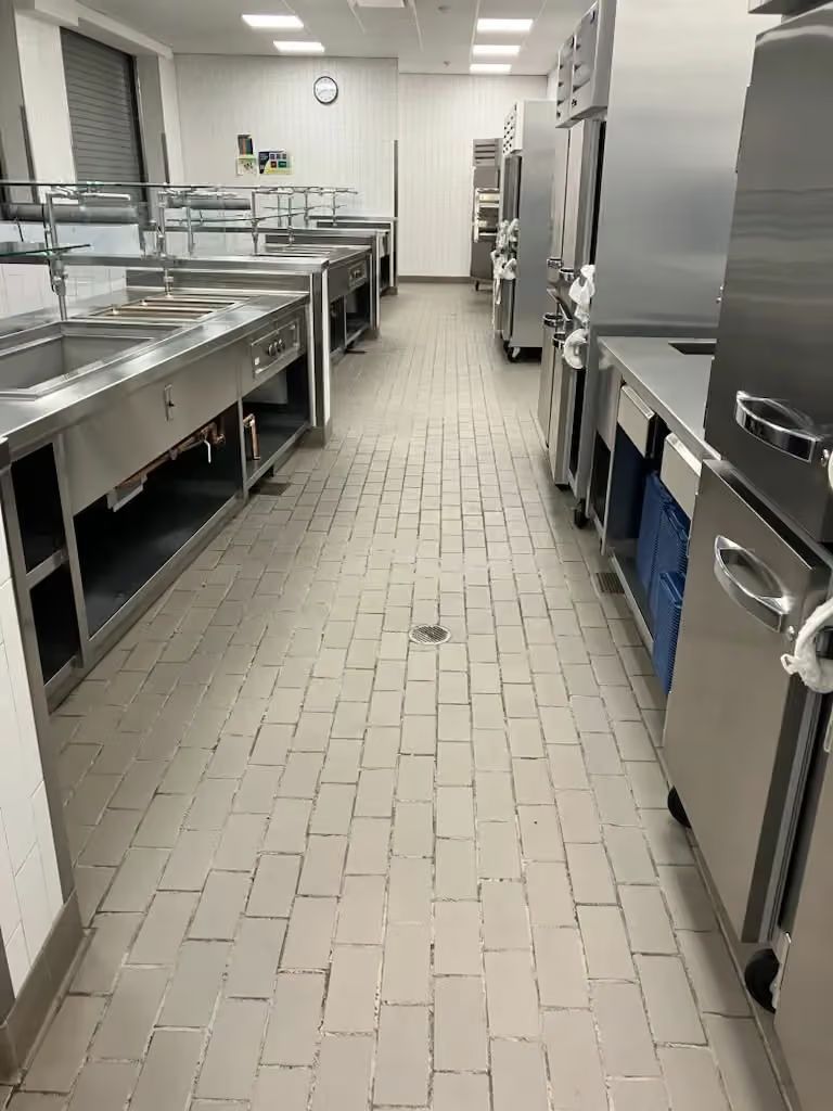 Commercial kitchen with stainless steel counters and appliances along a tiled aisle