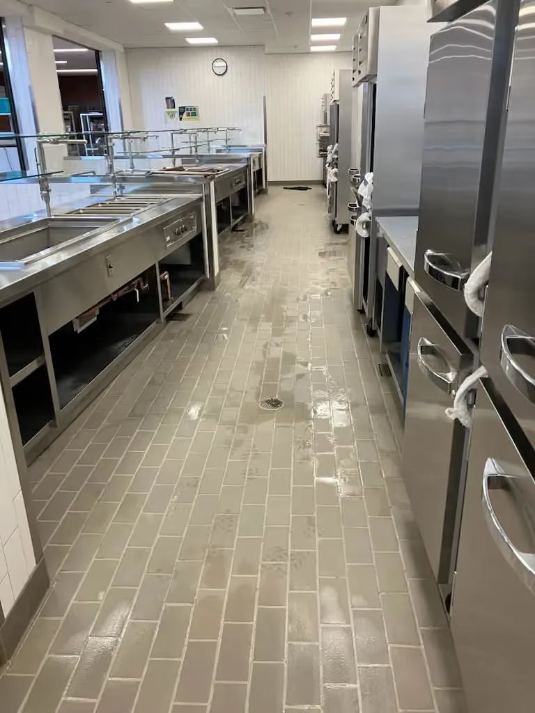 Commercial kitchen with stainless steel sinks, counters, and appliances lining a narrow tiled aisle.