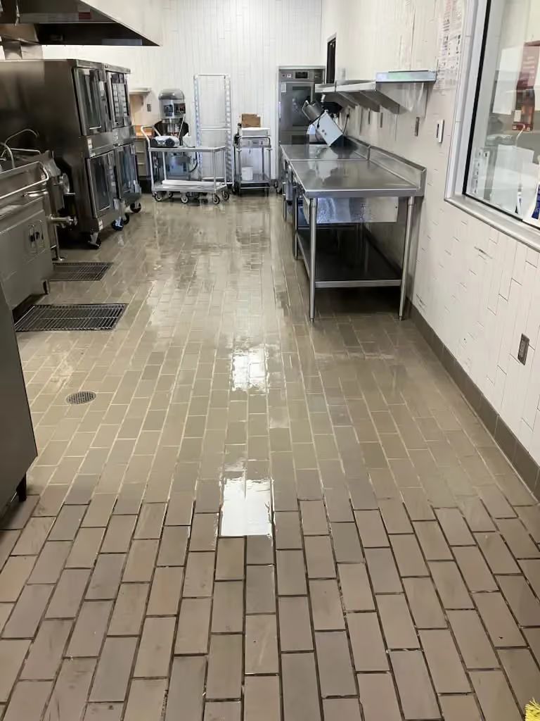 Empty commercial kitchen with stainless steel counters and a tiled floor.