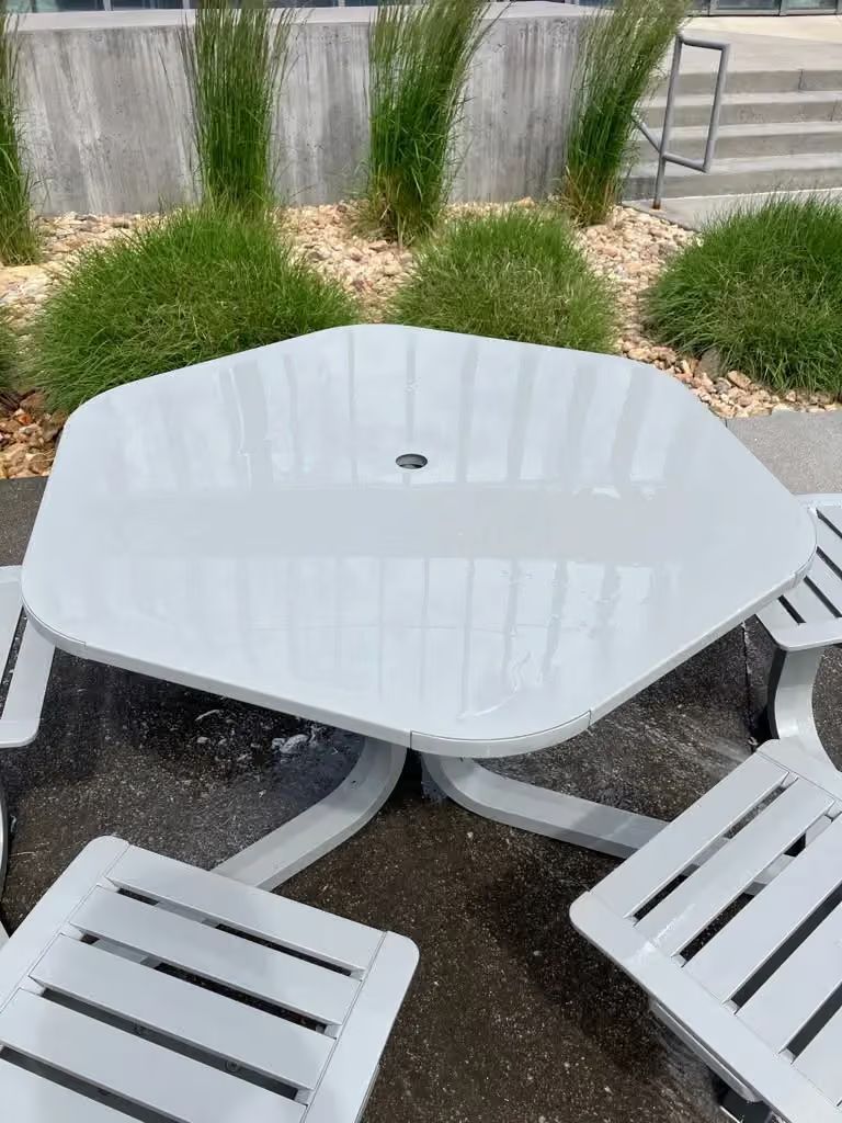 White patio table with slatted chairs on a wet outdoor deck beside a landscaped yard.