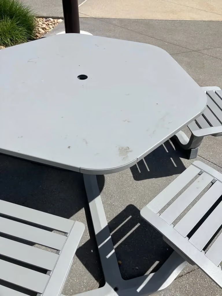 White outdoor patio table with four matching chairs in bright sunlight