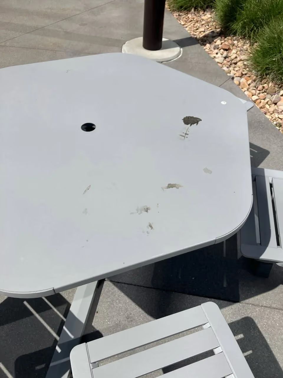 Gray outdoor patio table with chairs, shown from above on a sunny sidewalk patio.