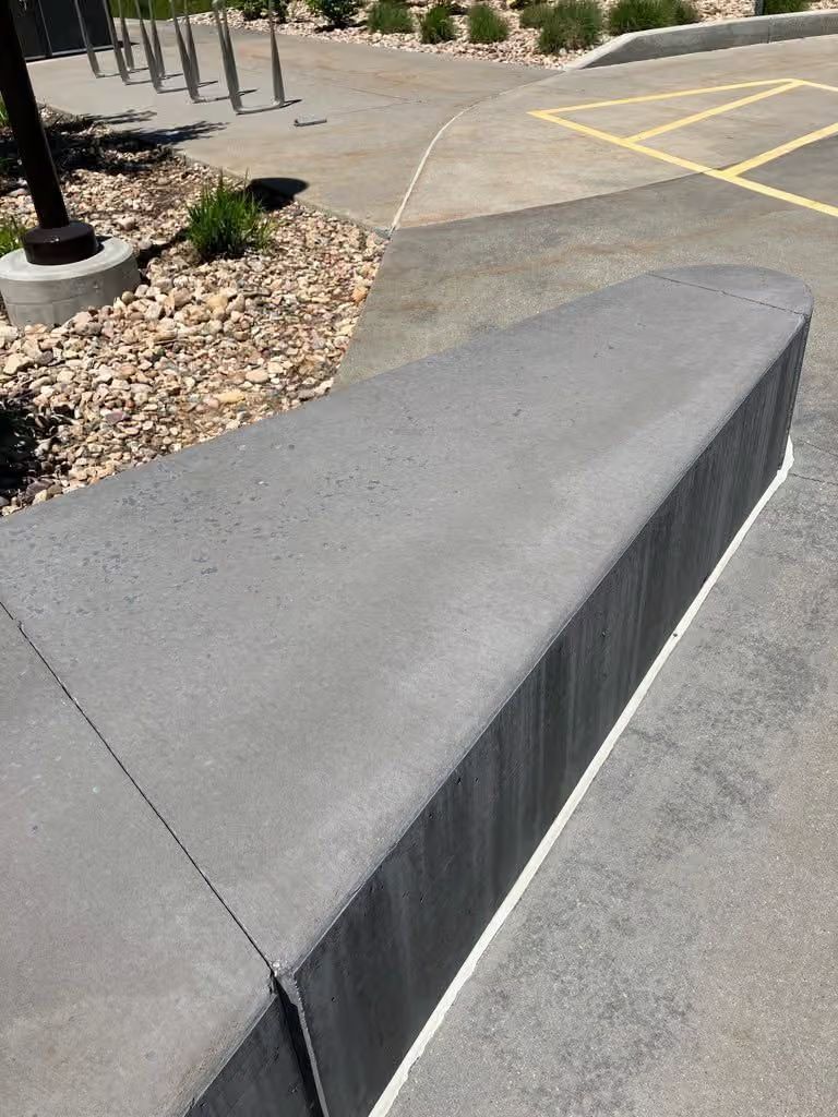 Concrete barrier along a parking lot walkway beside a landscaped area