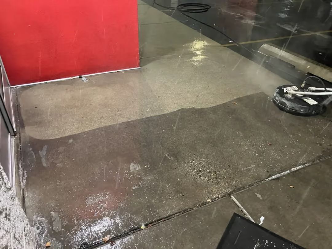 Wet concrete floor beside a red wall and glass door, with a small black scooter at right.