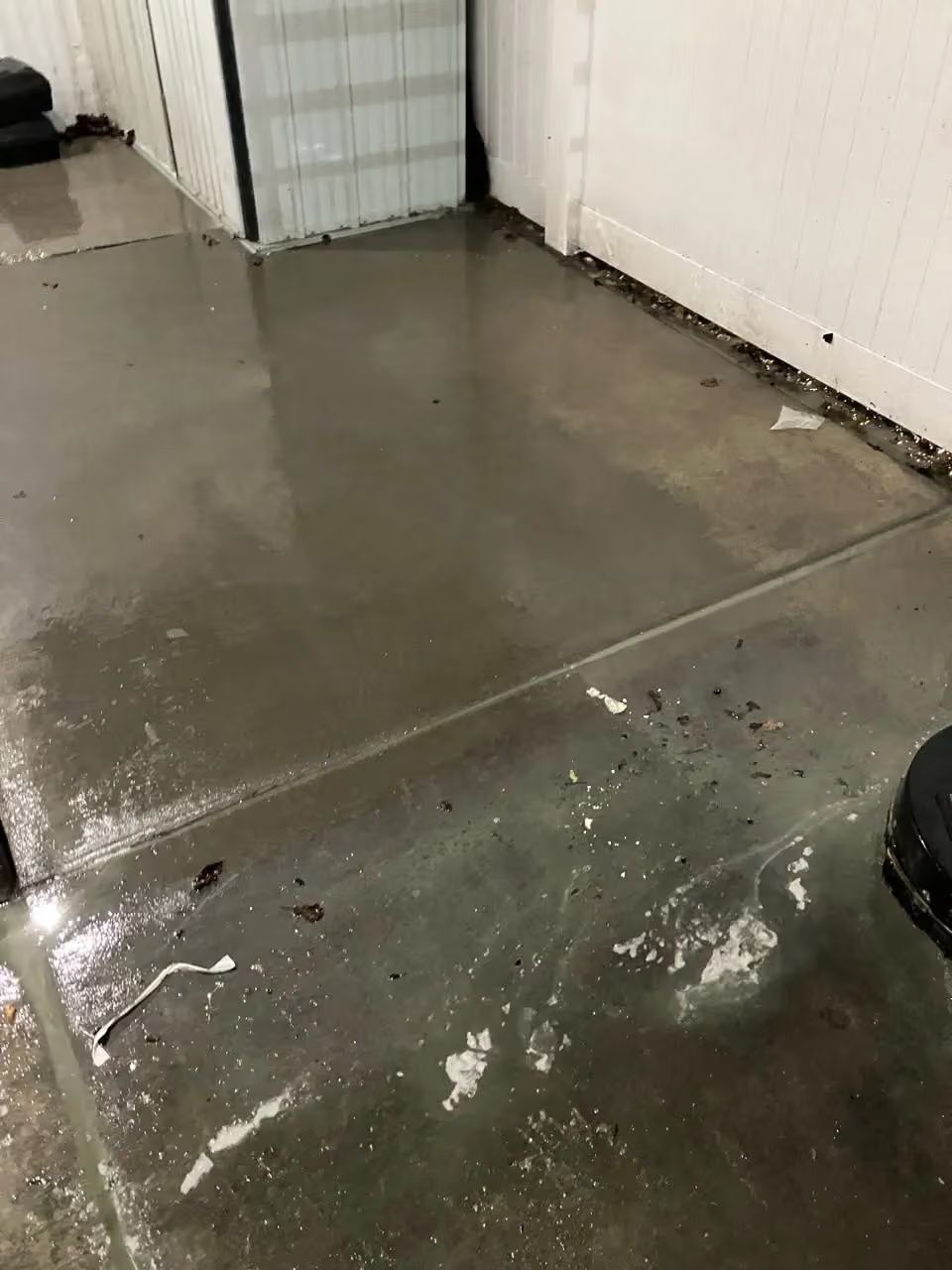 Wet concrete floor with a puddle and debris in a white-walled hallway
