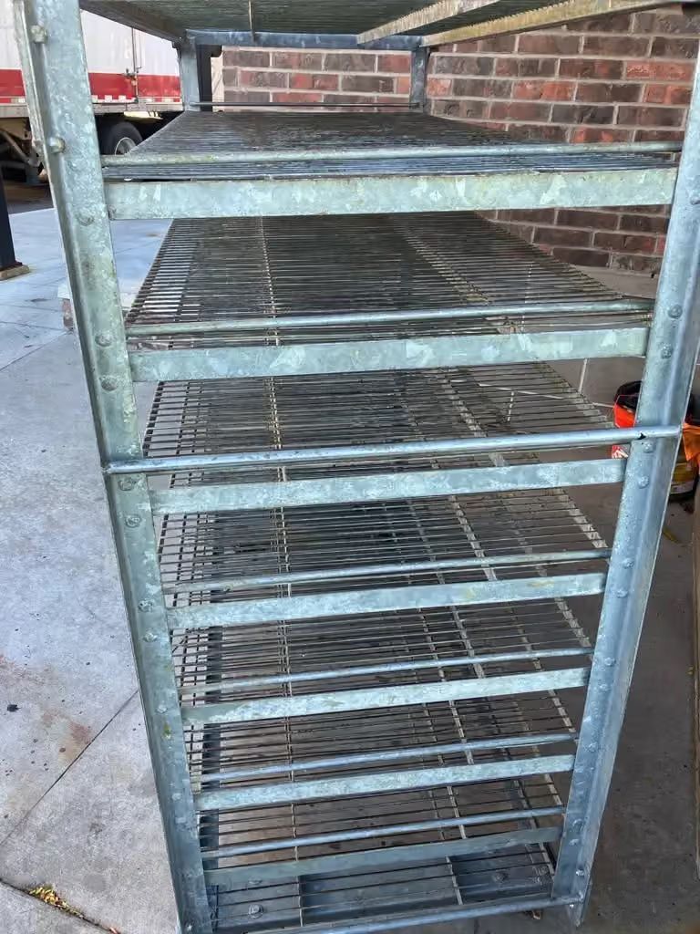 Metal wire rack with multiple shelves against a brick wall outdoors