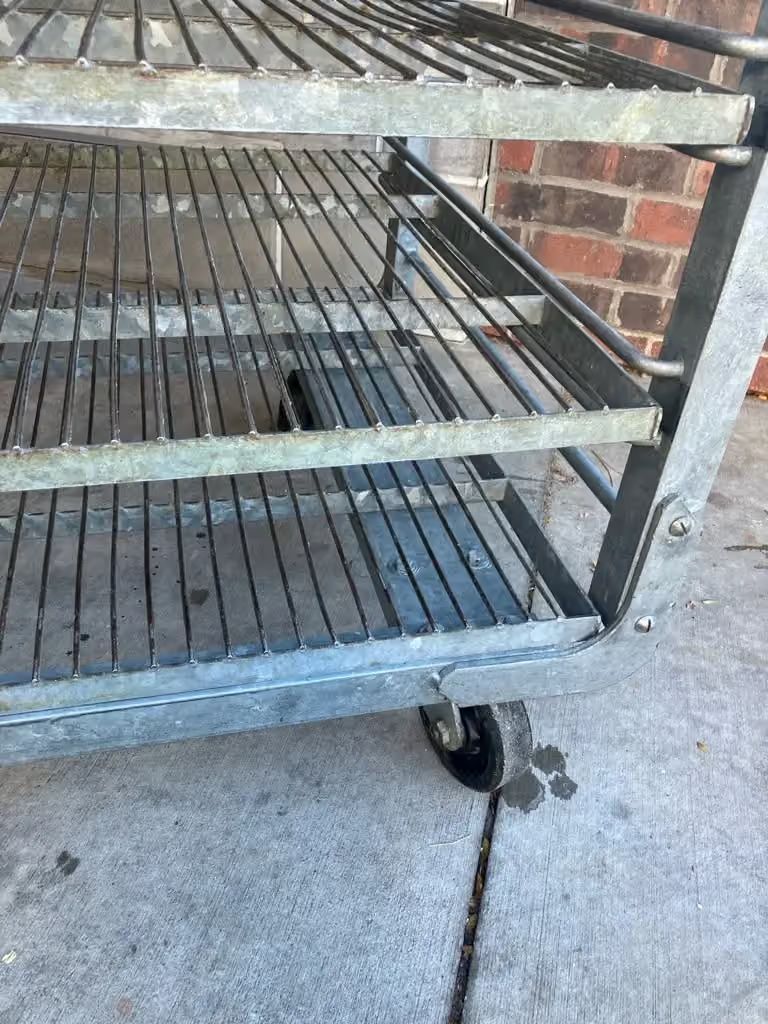 Black metal shopping cart with a broken wheel against a brick wall.