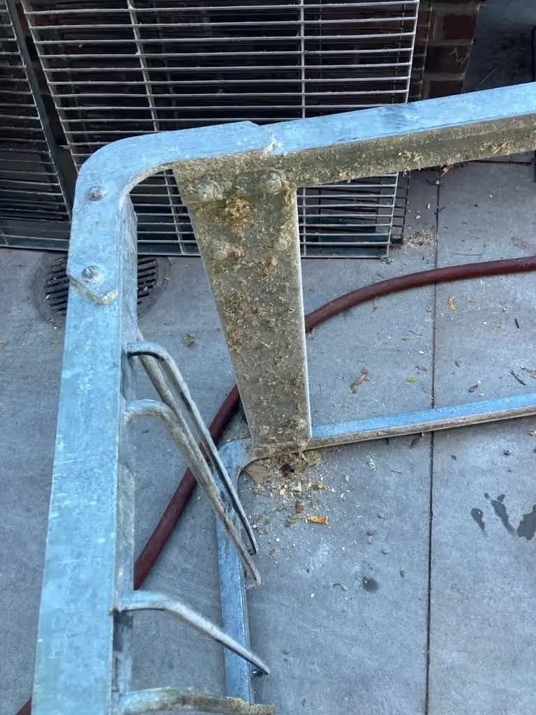 Weathered blue metal railing with rust and peeling paint beside an outdoor concrete area.