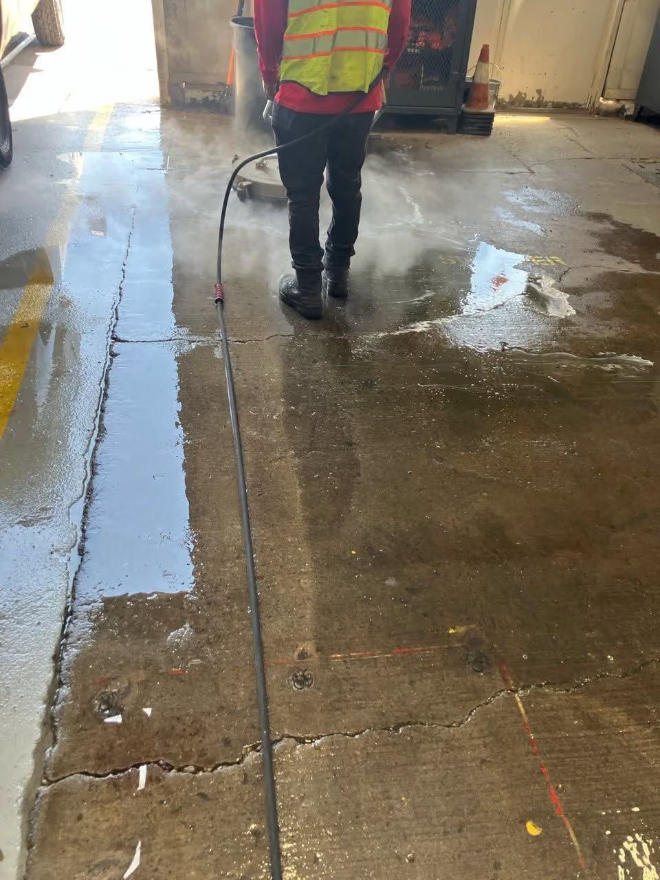 Worker in a neon safety vest spraying water on a wet concrete floor in an indoor industrial space