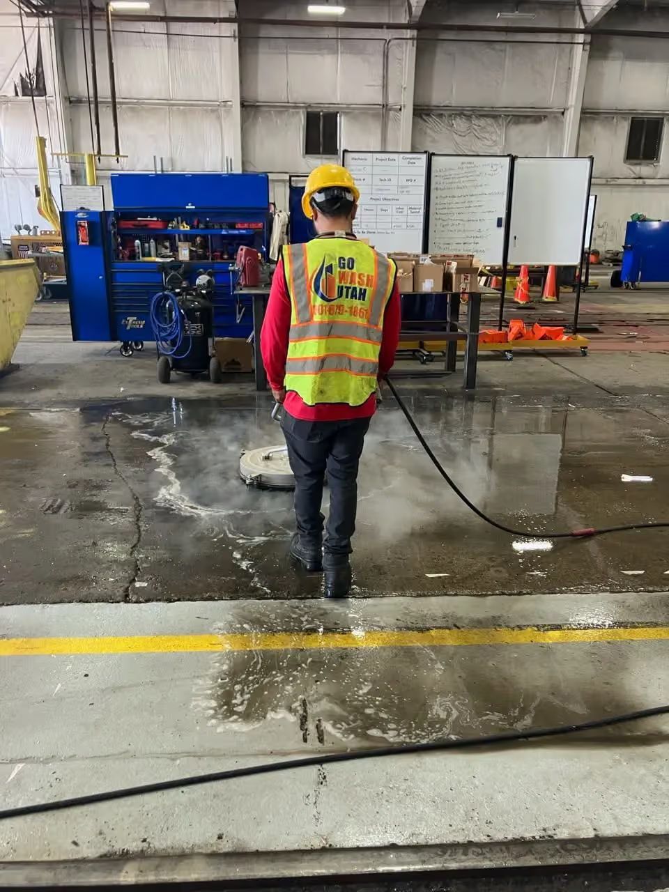 Worker in yellow safety vest and helmet walking in an industrial warehouse floor area.