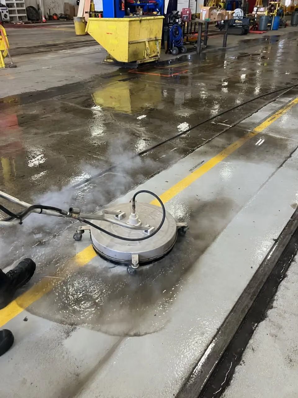 Industrial floor cleaning machine washing a wet concrete floor in a warehouse or garage area