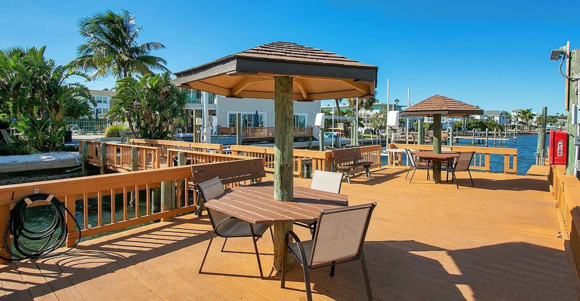 Outdoor dining area with tables, umbrellas, dock, and water views under a blue sky.
