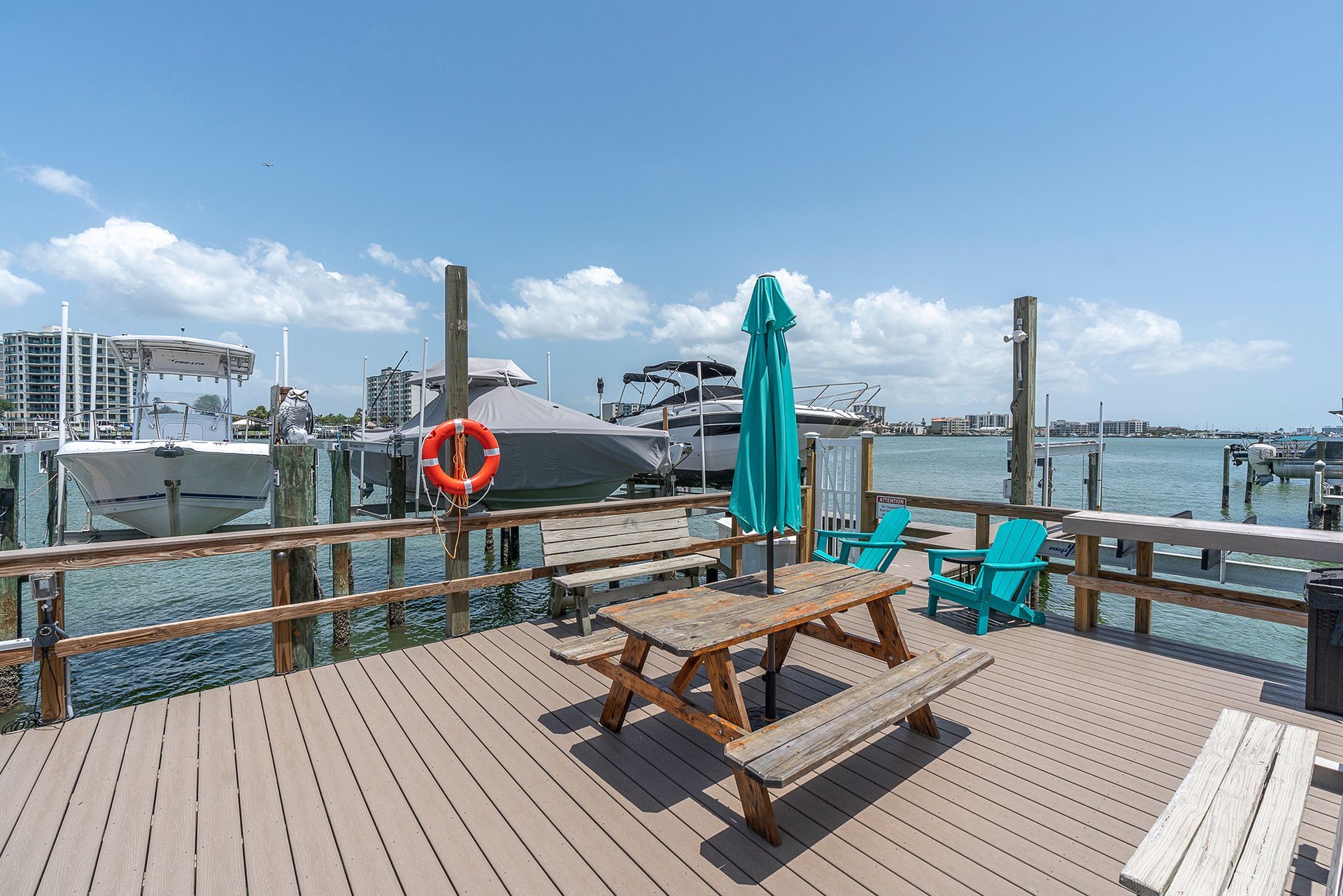Outdoor dining area with tables, umbrellas, dock, and water views under a blue sky.