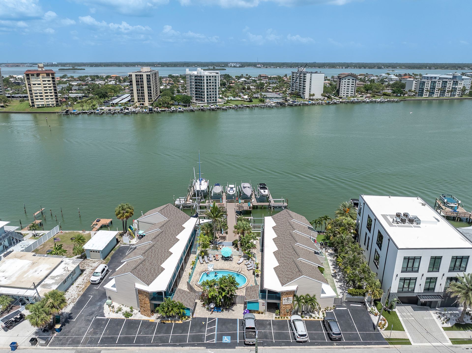 Aerial view of condos with a pool, near buildings and the ocean.