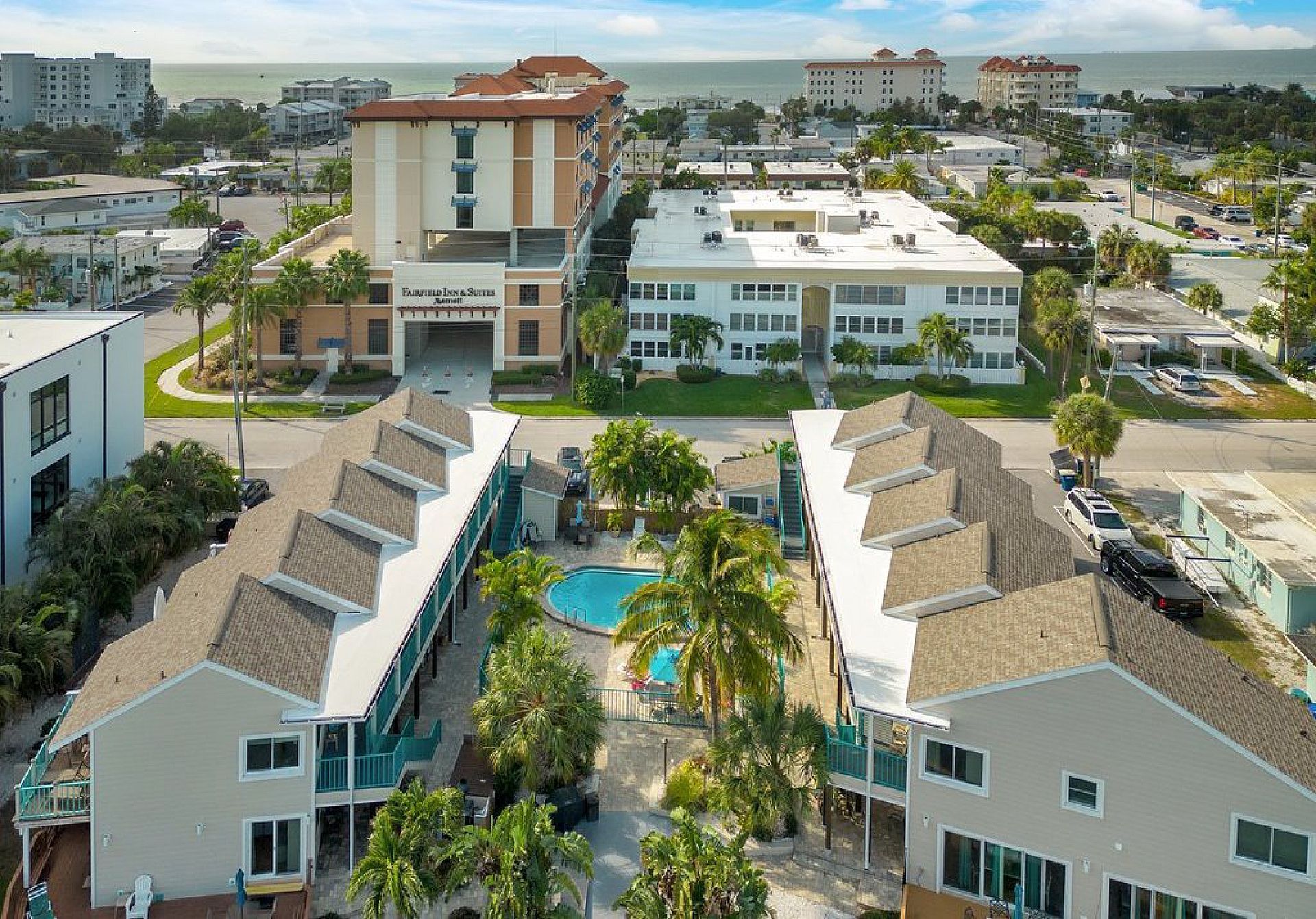 Aerial view of condos with a pool, near buildings and the ocean.