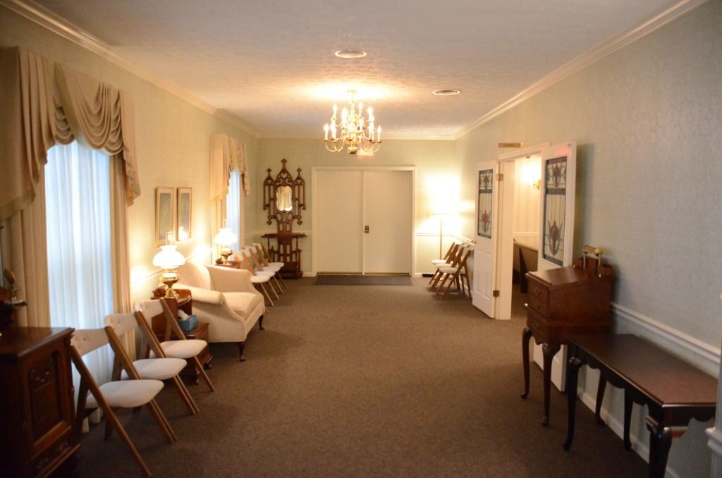 A long hallway with chairs , a table and a chandelier.