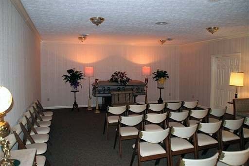 A room with rows of chairs and a coffin in the background.