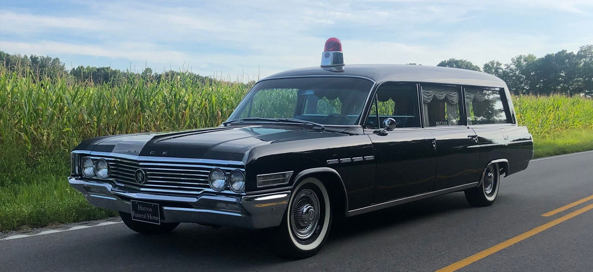 A black ambulance is driving down a road next to a field.