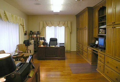 A living room with a desk , chairs , lamps and a computer.
