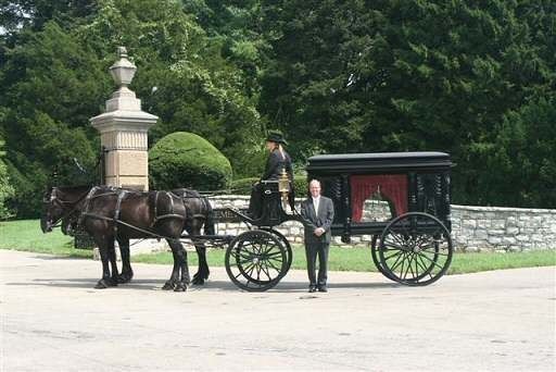 A man is standing next to a horse drawn carriage.