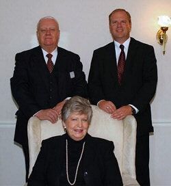 Three men in suits and ties are posing for a picture with a woman in a chair.