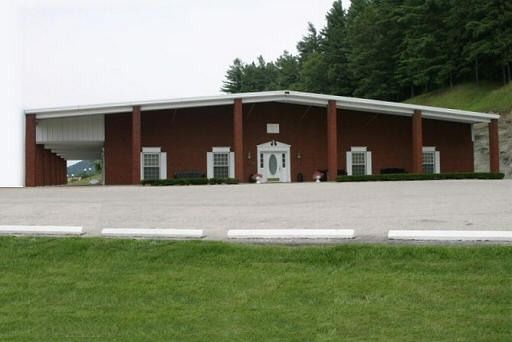 A large red building with a white roof is sitting in the middle of a grassy field.