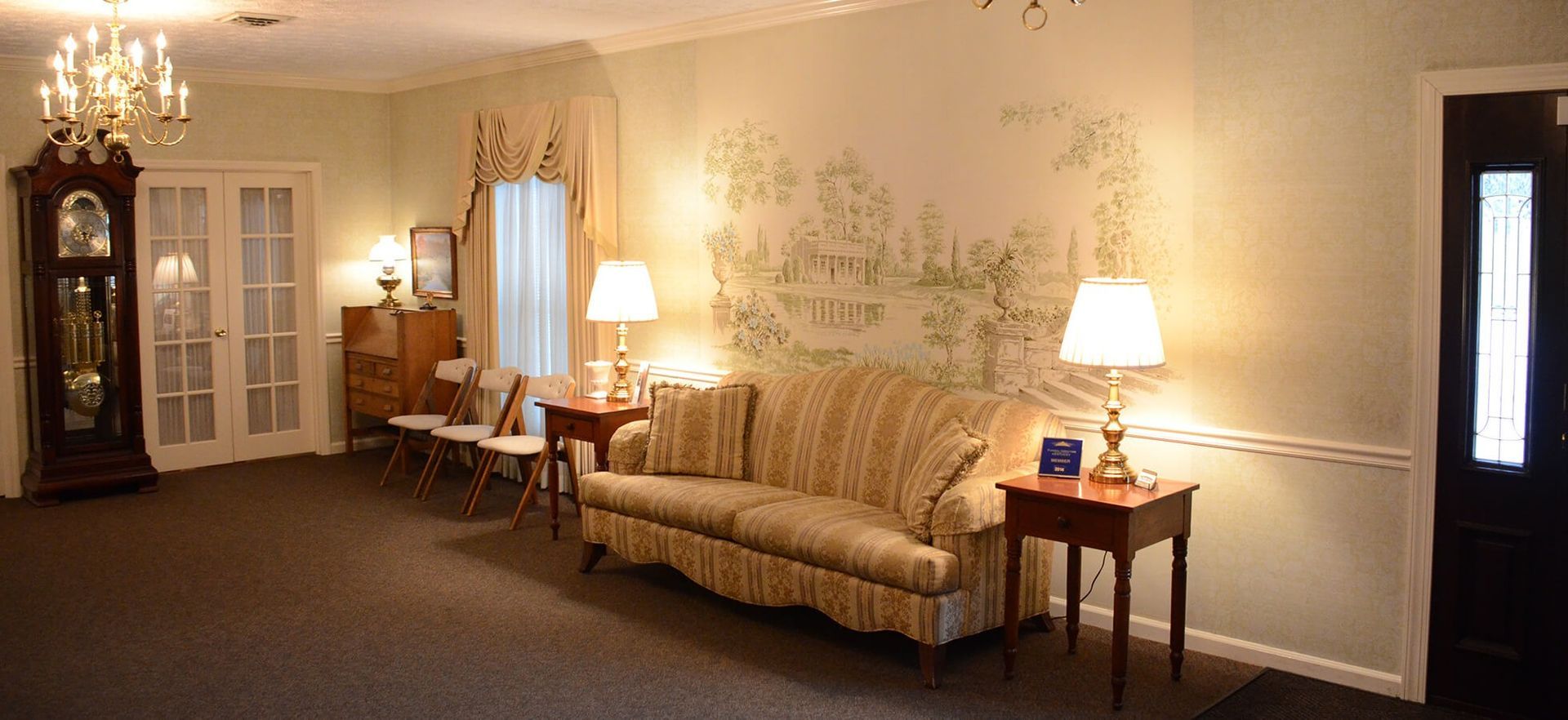 A living room with a couch , lamps , a clock and a chandelier.