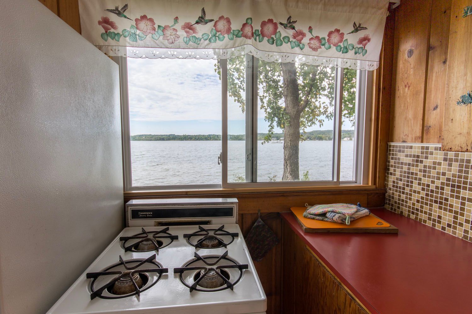 A kitchen with a stove and a window with a view of a lake