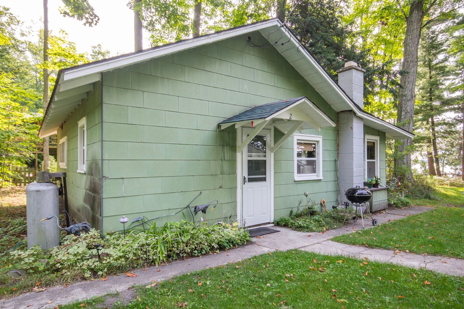 A small green house with a white door and a grill in front of it