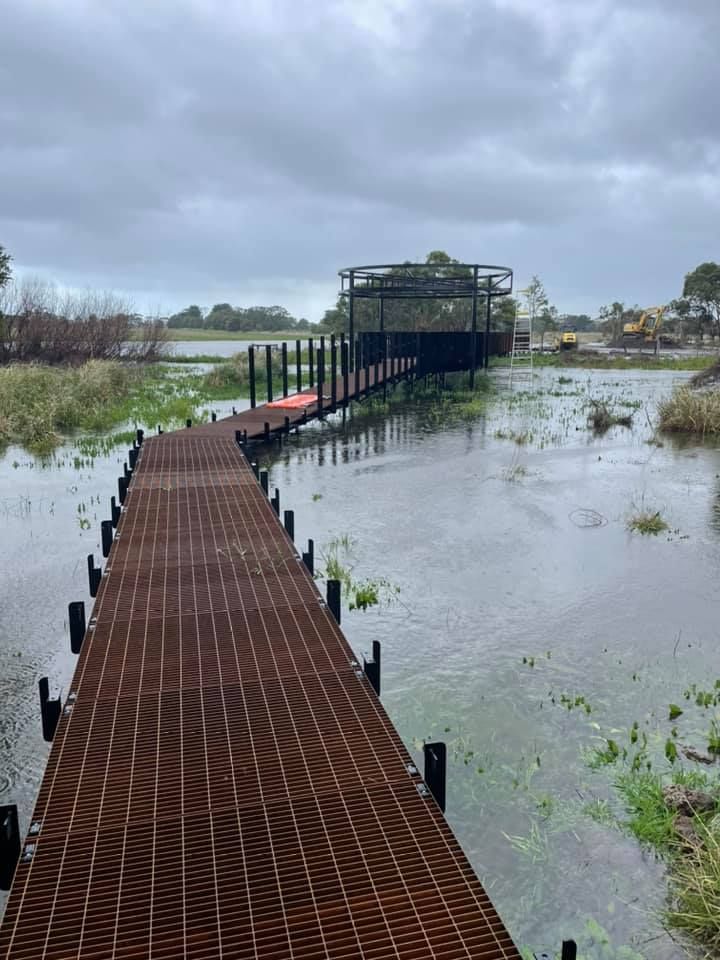 A wooden dock leading to a flooded river on a cloudy day.
