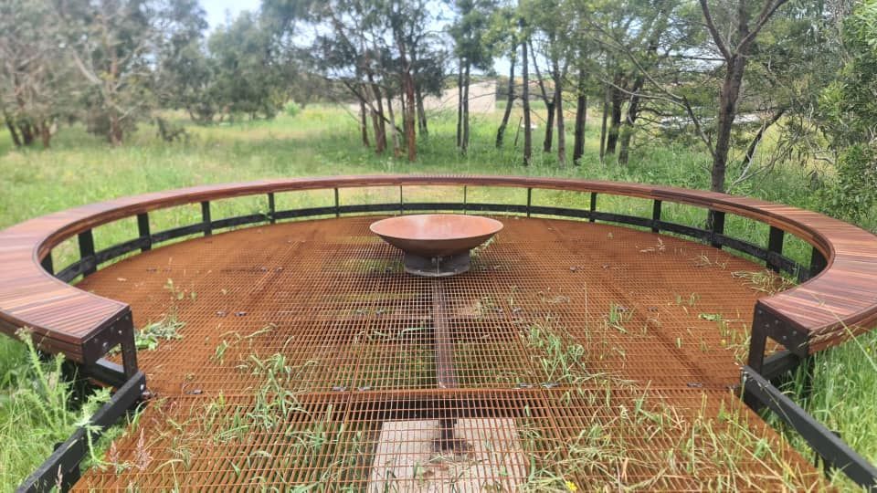 A wooden bench with a fire pit in the middle of a field.