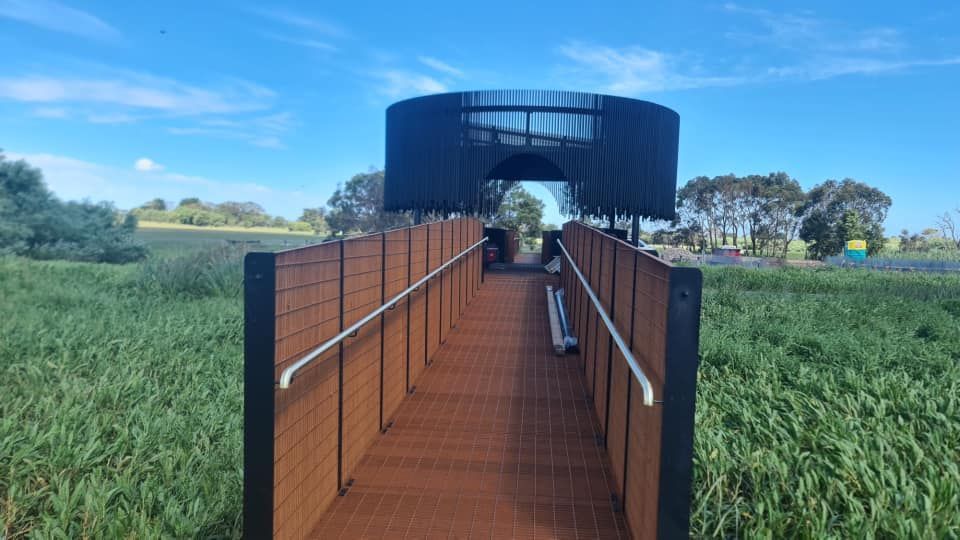 A wooden walkway leading to a tower in the middle of a field.
