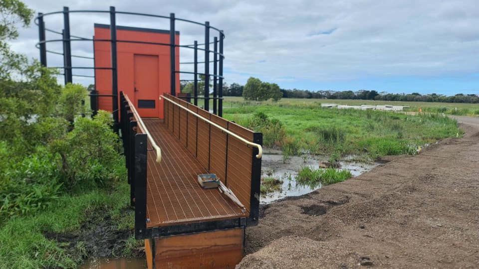 A wooden bridge leading to a red door in a field.
