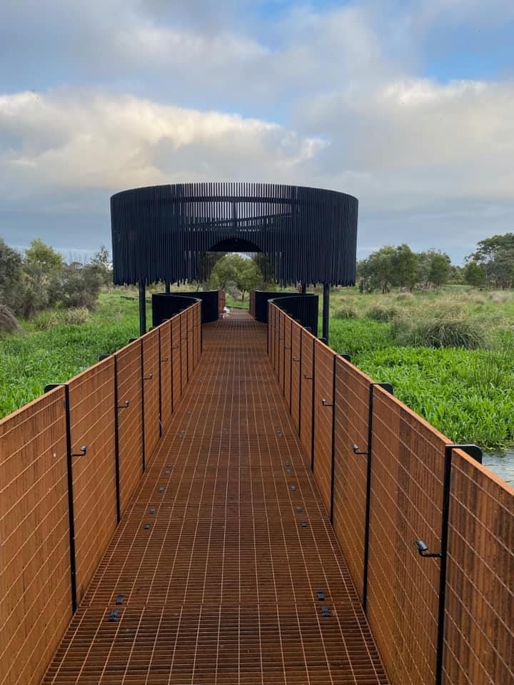 A long wooden walkway leading to a building in the middle of a field.