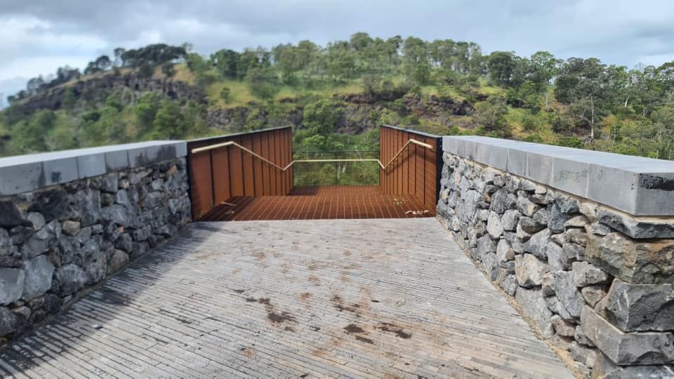 A stone wall with a wooden walkway leading to a bridge over a river.