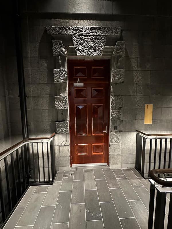 A dark hallway with a wooden door and a brick wall