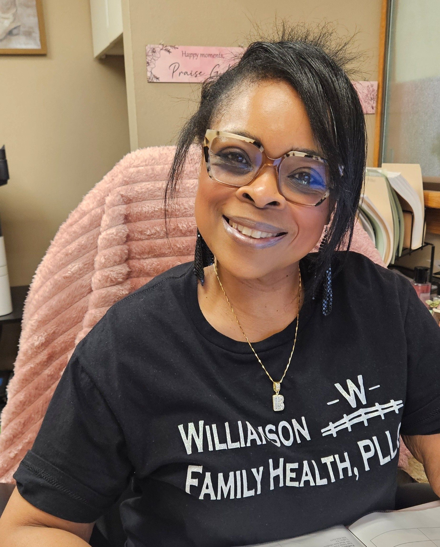 Woman with short black hair smiles wearing red and black plaid shirt, red earrings, indoors.
