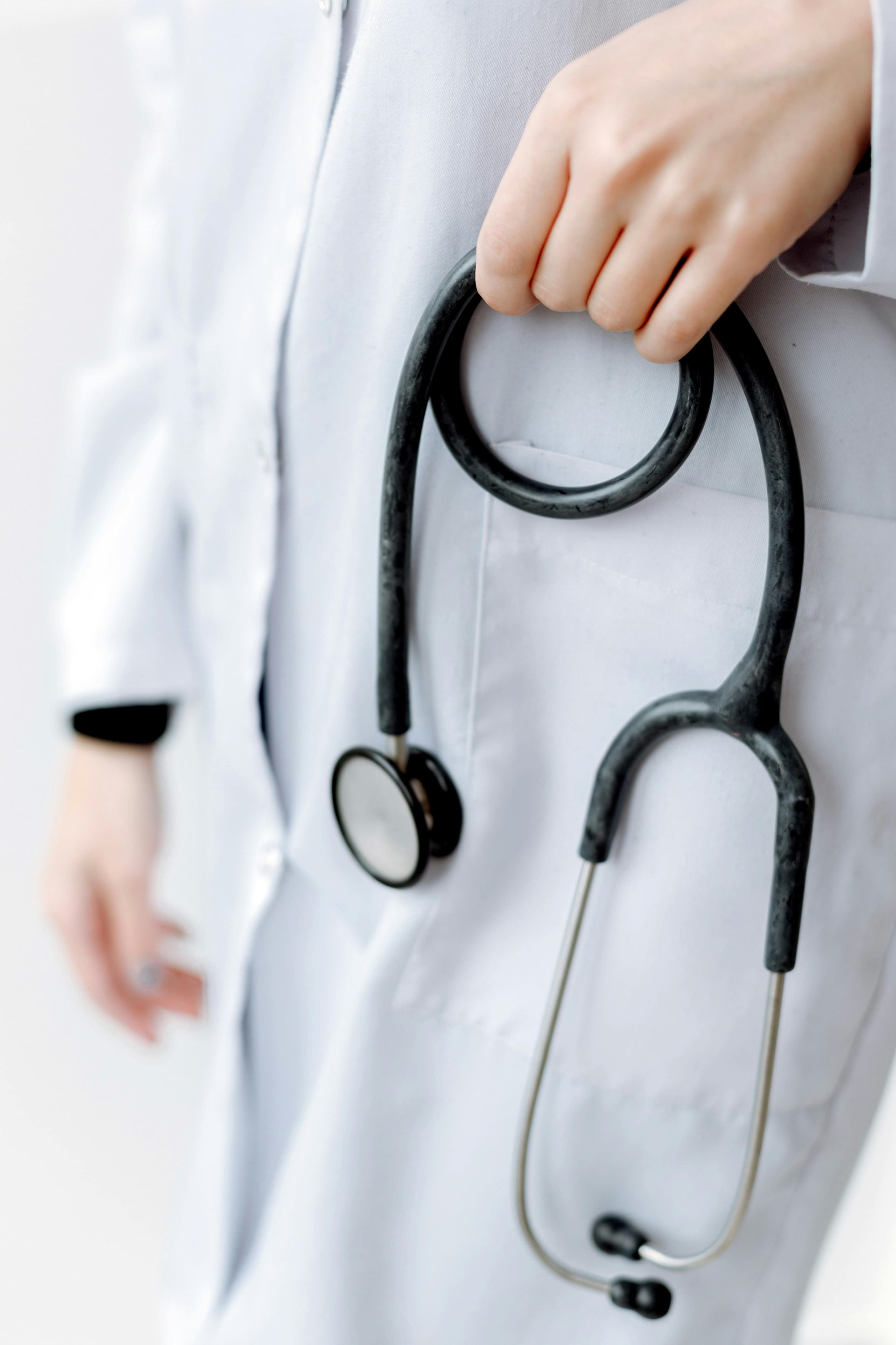 Person in a white coat holding a black stethoscope.