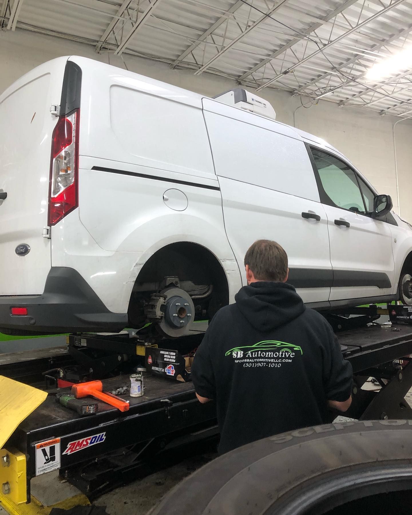 Mechanic working on a white van lifted in a garage. The van's wheel is removed, showing the brakes. | SB Automotive