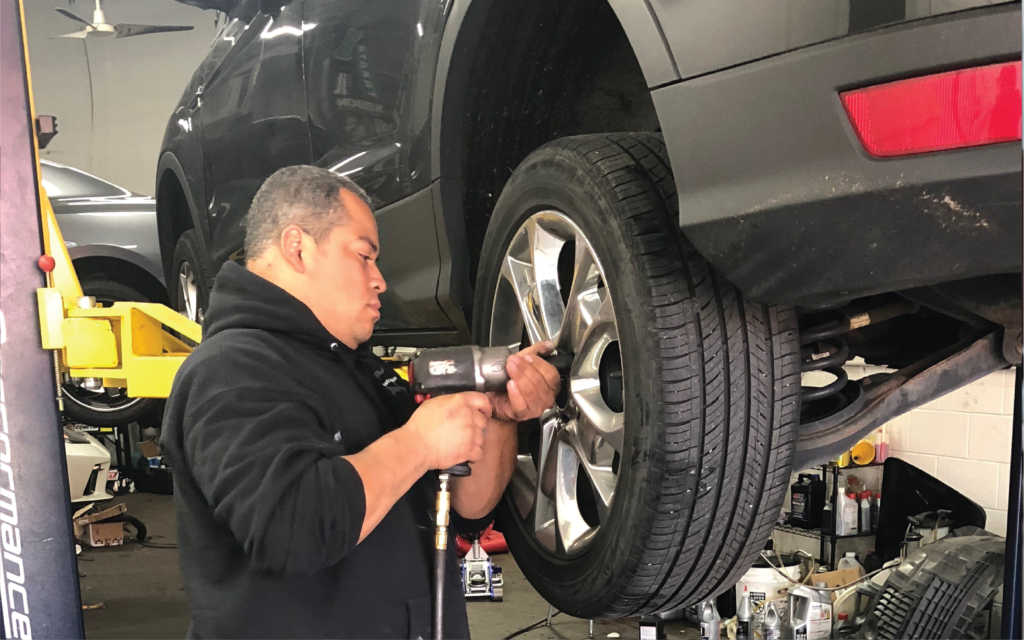 Mechanic using a power tool to remove a tire from a car in a garage. | SB Automotive