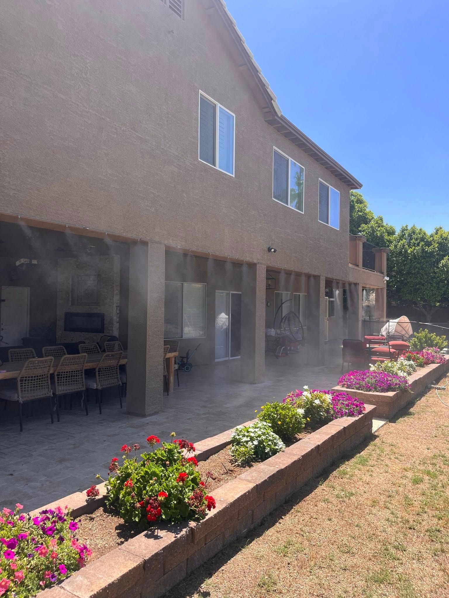 Two-story stucco house with covered patio and flower bed along the side yard.