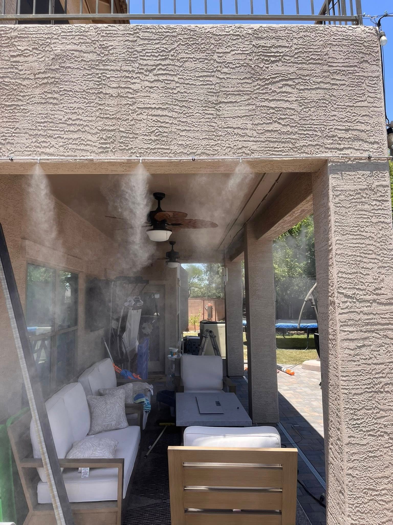 Covered patio with outdoor seating, a ceiling fan, and mist spraying near the back wall.