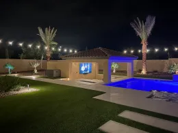 Modern backyard at night with lit pool, palm trees, lawn, and house patio lights