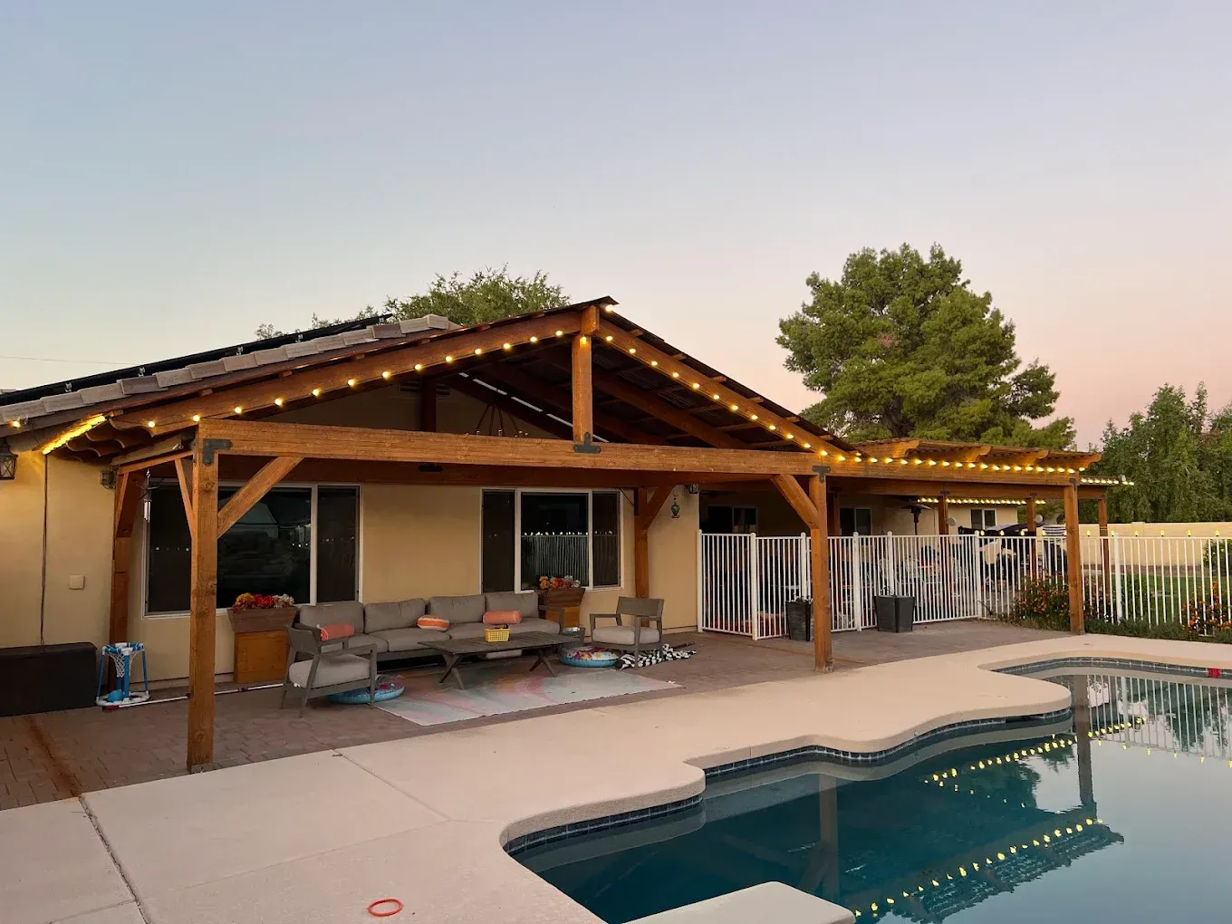 Backyard patio with a wooden pergola beside a swimming pool at sunset
