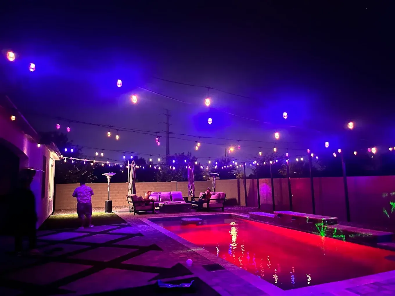 Purple-lit outdoor pool patio with string lights and a glowing red pool at night